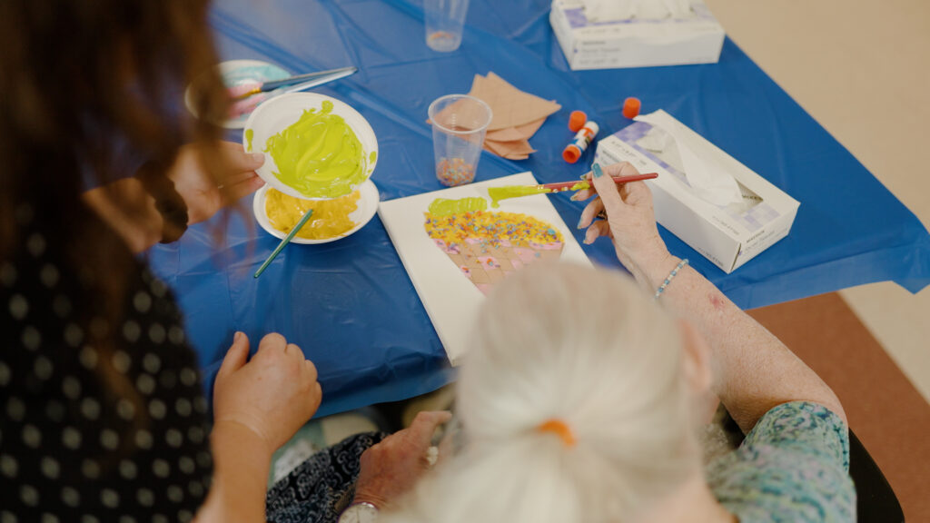 A woman is painting with a nurse as an activity at a skilled nursing center
