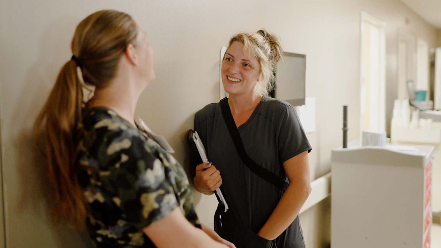 Two nurses smiling and talking in a hallway of a skilled nursing facility