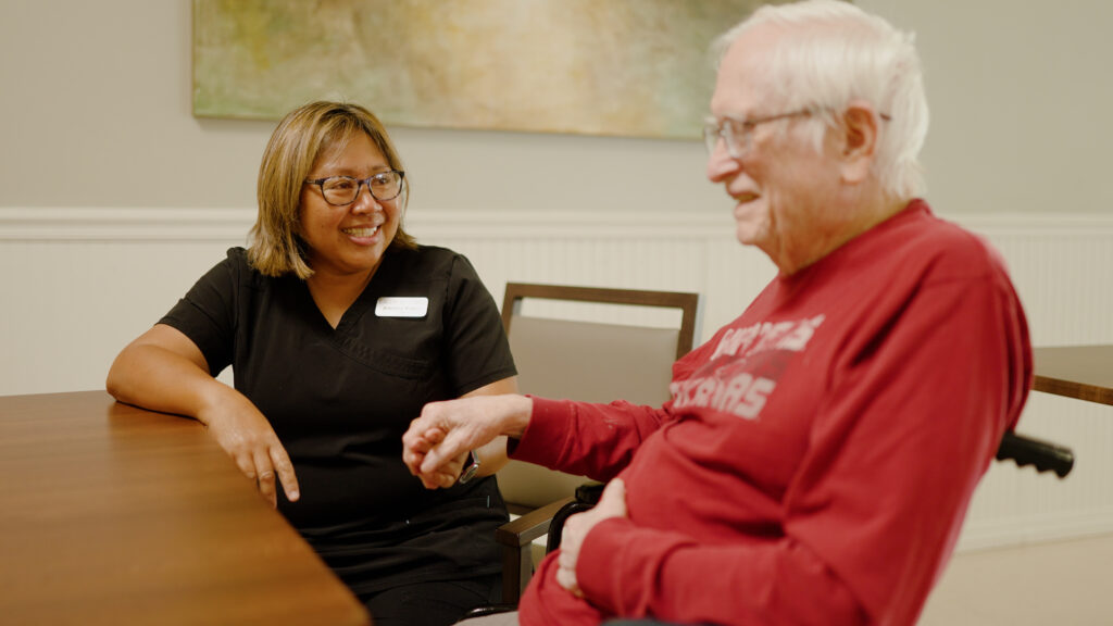 A man and a nurse are smiling at talking at a skilled nursing facility